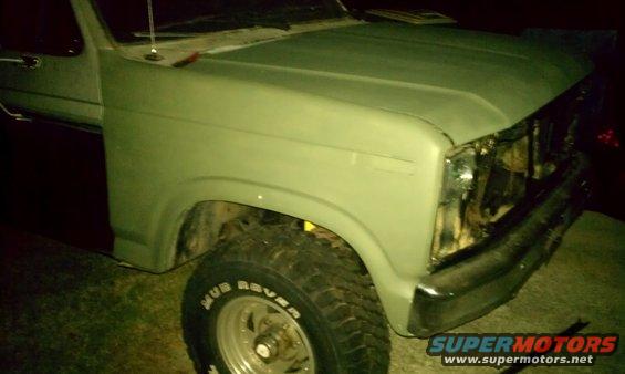 Front fender, headlight area, and tire of a light green Ford Bronco. The grille is missing