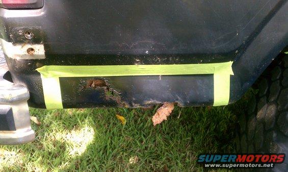 Black vehicle rear quarter panel with rust hole covered by green tape