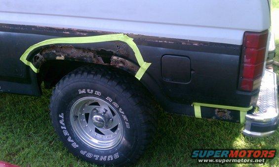 Side view of a 1985 Ford Bronco with rust around the rear wheel well, taped off for repair