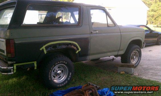 Green Ford Bronco with black rear quarter panel, taped for repair, on grass