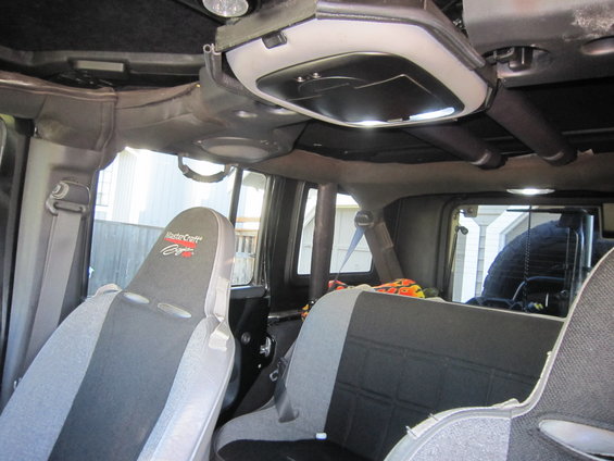 Interior view of a Jeep Wrangler showing front MasterCraft seats and rear bench seat. Spare tire visible through rear window