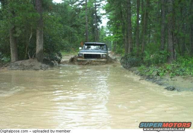 Dark SUV driving through mud and water in a forest