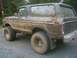 1979 Ford Bronco - This heavily mud-splattered SUV is viewed from the front-three-quarter angle, revealing its off-road modifications.