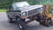 1979 Ford Bronco - A forklift is lifting the front end of a dark green Ford Bronco, showing its lifted suspension.