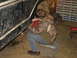1979 Ford Bronco - A person works on the underside of a vehicle that is supported by a red jack in a garage.
