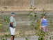 2006 Ford E350 - Two individuals stand in front of a wooden retaining wall with dry grass and foliage in the background.