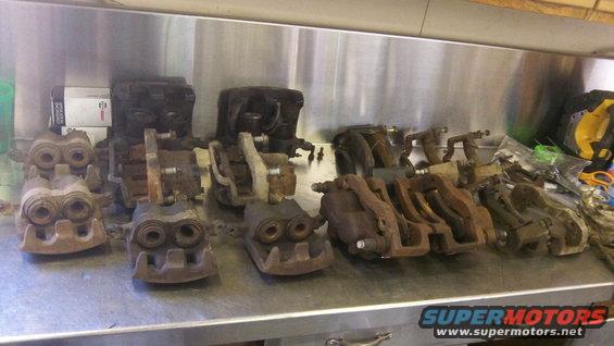 Row of various used brake calipers on a metal workbench