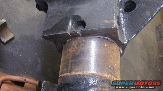 Close-up of a rusty metal cylinder attached to a black bracket with visible welds