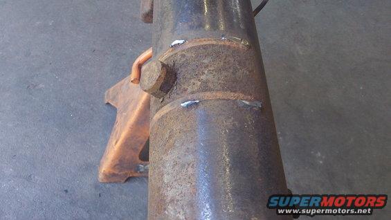 Close-up of a rusty, welded axle housing supported by an orange jack stand