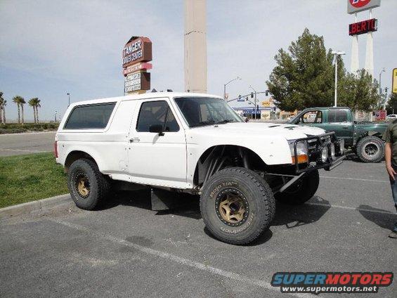 White 1995 Ford Bronco modified for off-road use, parked in a lot with a green pickup truck behind it