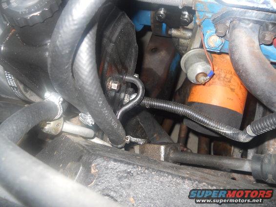 Engine bay showing hoses, oil filter, and metal components. Some text visible on filter