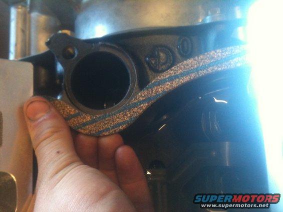 Hand holding a gasket against a dark engine component with visible casting marks