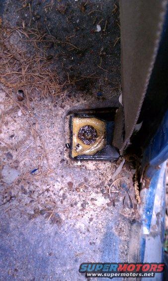 Seatbelt anchor point on a dirty vehicle floor with debris and a visible SuperMotors logo