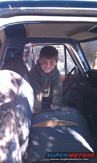 Interior view of a blue vehicle with a young boy, showing torn seats