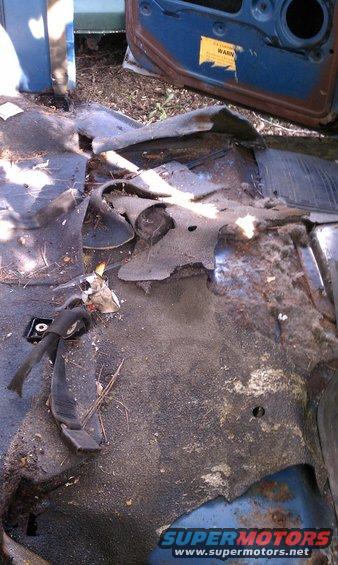 Interior floor of a vehicle with torn carpet and rust visible