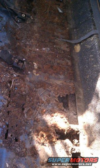 Rusted interior floor pan with debris and holes, viewed from above