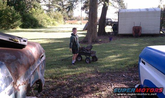 Rusty vehicle parts in a yard with a boy and a wagon