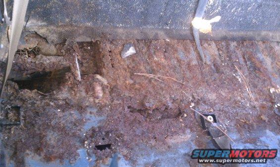 heavily rusted interior floor pan with holes and debris
