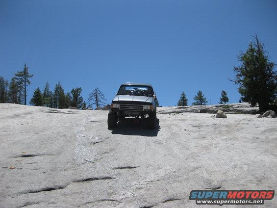 Silver SUV with large tires on a rocky, uneven terrain under a clear blue sky