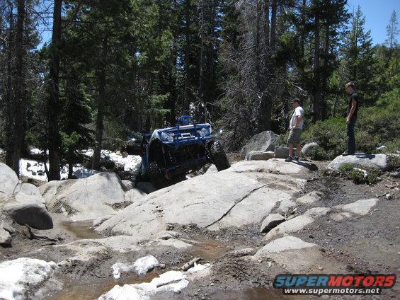 Blue off-road buggy climbing over large rocks on a wooded trail