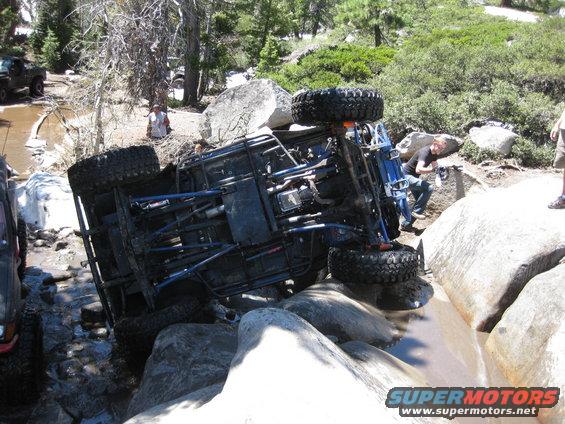 Overturned off-road vehicle on rocks in a stream, with another vehicle visible to the left
