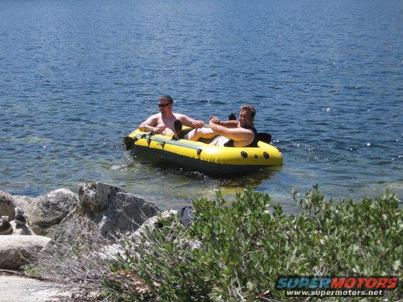 Two men relax in a yellow inflatable boat on a blue lake