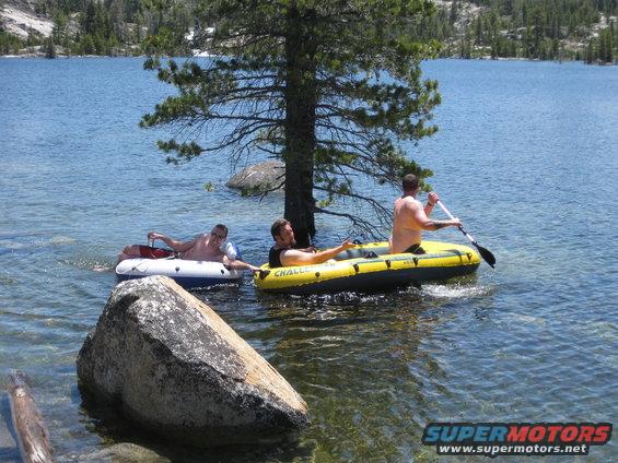 three guys in inflatable boats on a lake, one paddling