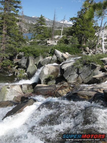 Mountain lake and stream with rocks and trees under a blue sky