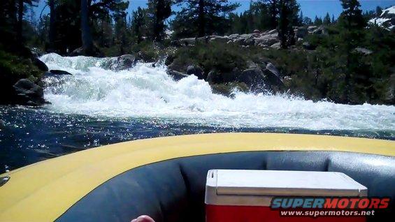 Rafting down a river with rapids and trees on the bank. Cooler in the raft