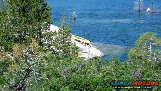 Yellow kayak resting on a rock near blue water, surrounded by trees and bushes