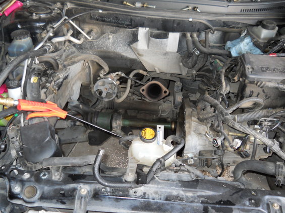 Engine bay with various hoses, wires, and engine components visible. An orange air duster is pointed towards the center