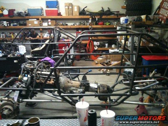 Custom buggy frame with engine and transmission, two vehicles in garage