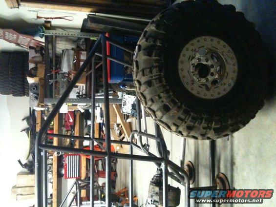 Off-road buggy frame with large tire, unfinished construction, in garage