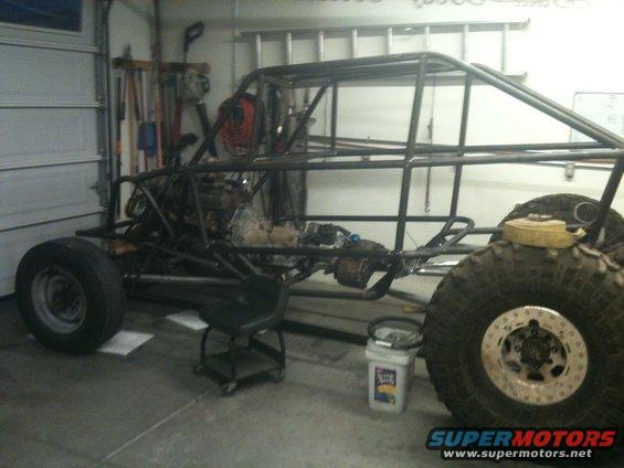 Side view of a custom buggy frame with engine and large tires, in a garage