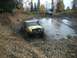 1979 Ford Bronco - Two off-road vehicles navigate a muddy trail with trees and fallen leaves.