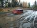 1979 Ford Bronco - A red Jeep Wrangler navigates a challenging muddy terrain, with its front-right wheel deep in the mire.