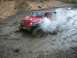 1979 Ford Bronco - A red Jeep Wrangler navigates a muddy trail, creating a cloud of smoke as it churns through the mire.