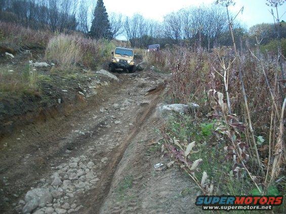 Yellow Jeep Wrangler climbing a rocky, muddy trail with another vehicle behind it