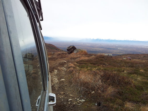 View from inside a vehicle looking out at a landscape with another vehicle stuck on a rock and a few more in the distance