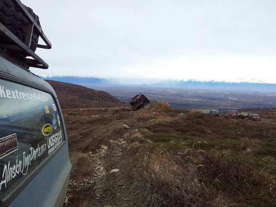 Off-road vehicles on a mountain trail with a crashed vehicle in the distance