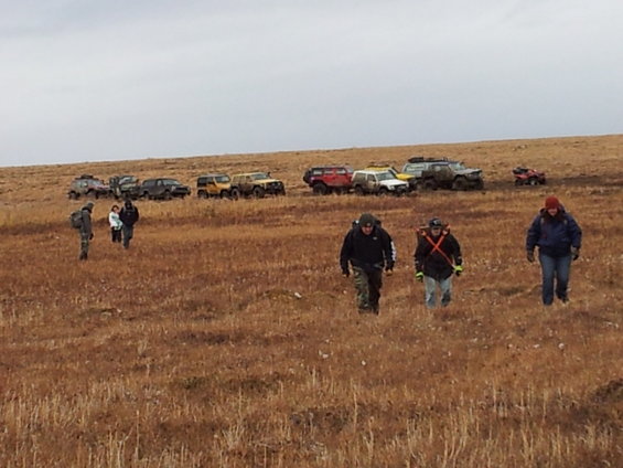 Group of off-road vehicles parked on a hill with people walking in the foreground