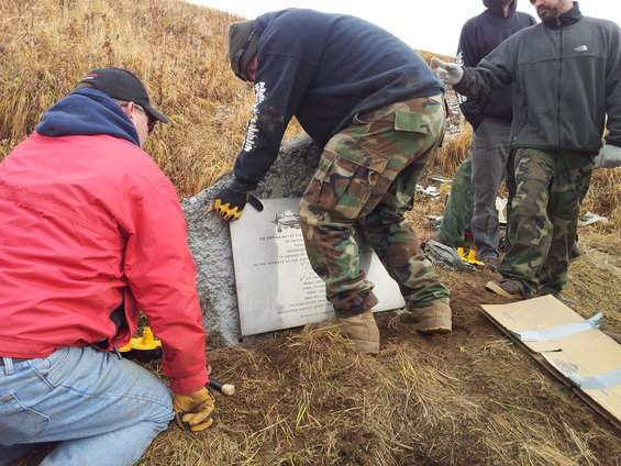 People installing a memorial plaque with an airplane illustration on a grassy hill