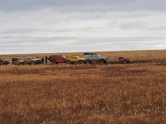 Gray SUV with roof rack and other off-road vehicles in a line on a dry, grassy plain