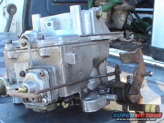 Metal carburetor with linkage and yellow-capped lever, resting on a surface