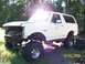 1989 Ford Bronco - A white 1989 Ford Bronco sits on a grassy lot with its front end disassembled.