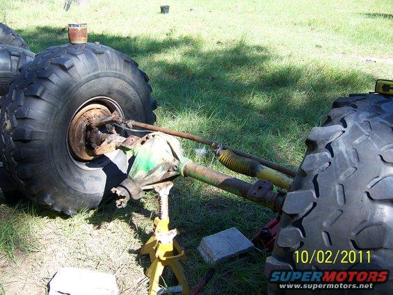 Vehicle axle with large tire, supported by a jack. Green and yellow components visible