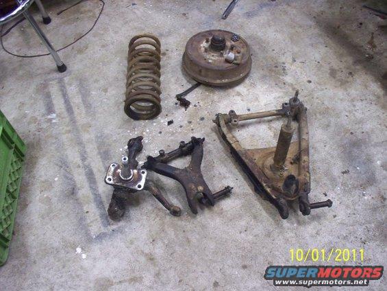 Rusty car suspension parts including a coil spring, brake drum, and control arms on a concrete floor