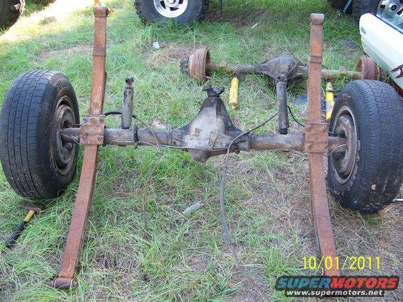Vehicle rear axle with leaf springs and tires. Another axle is visible behind it