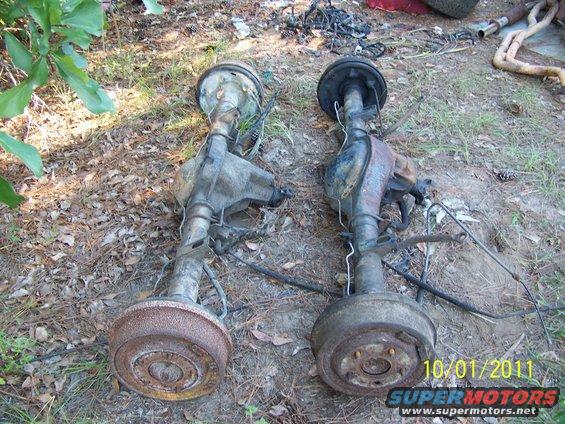 Two rusty rear axle assemblies with drum brakes lie on the ground