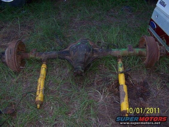 Rear axle assembly with two yellow shock absorbers lying on grass